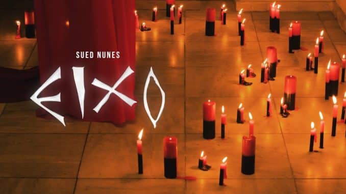 Capa do videoclipe "EIXO" de Sued Nunes Imagem promocional do videoclipe "EIXO" de Sued Nunes, com velas vermelhas e pretas acesas no chão em um ambiente sombrio, com o título do clipe em destaque.